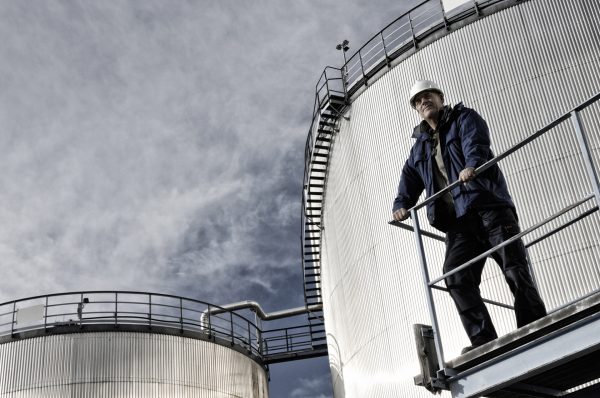 oil worker engineer with giant fuel storage towers in background BYLsHBC4s